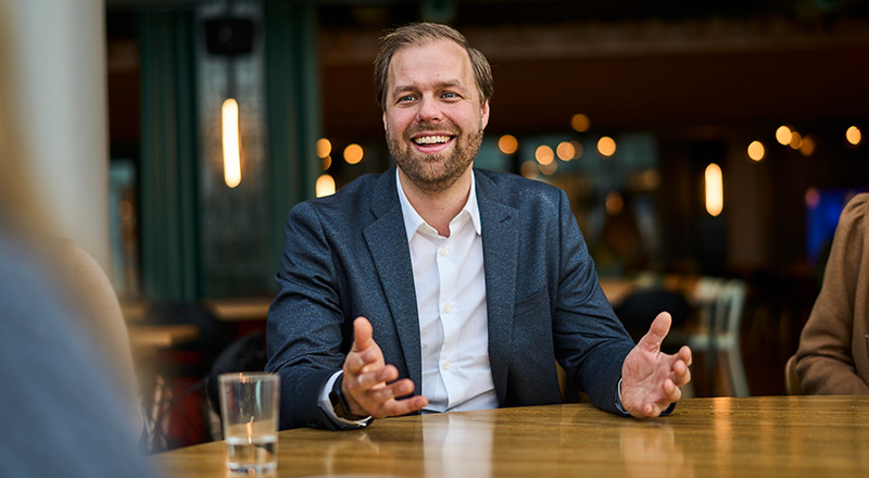 Erlend Gjaere con los brazos abiertos se muestra sonriente en una mesa con un vaso de agua